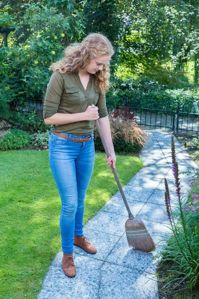Young dutch woman sweeps garden path with wicker broom — Stock Photo, Image