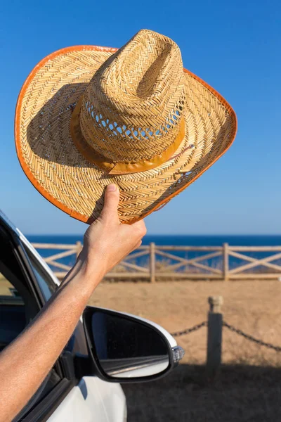 Ramię w samochód posiadający słomkowy kapelusz na wybrzeżu — Zdjęcie stockowe
