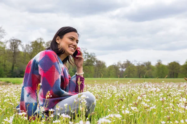 Mulher senta-se em florescente prado telefonando móvel — Fotografia de Stock