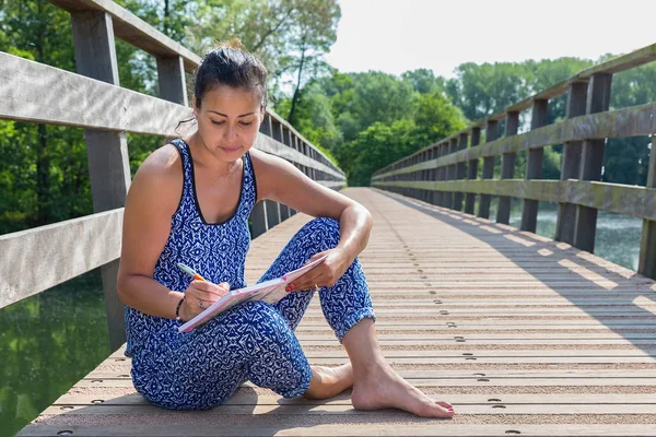 Mujer se sienta a escribir en puente de madera —  Fotos de Stock