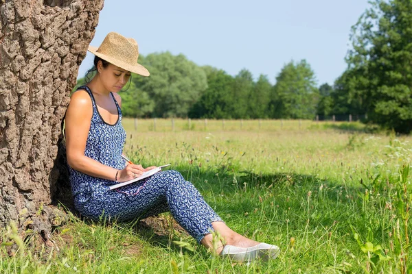 Mujer sentada contra el árbol escribiendo en la naturaleza —  Fotos de Stock