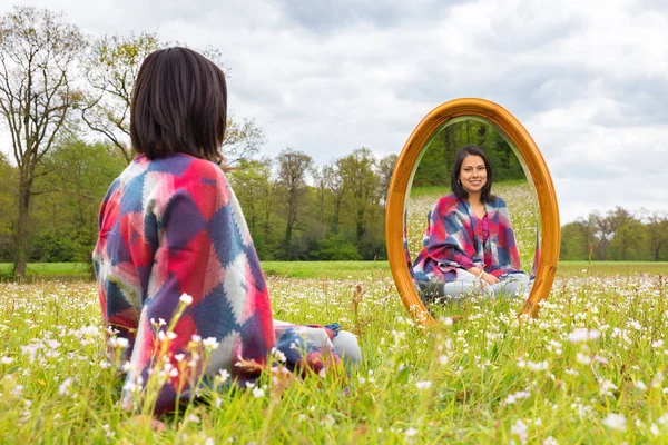 Vrouw zitten met spiegel in bloeiende weide — Stockfoto