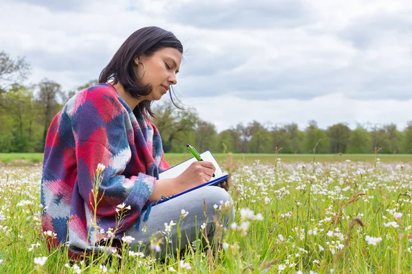 Mujer escribe en el prado con flores de primavera —  Fotos de Stock