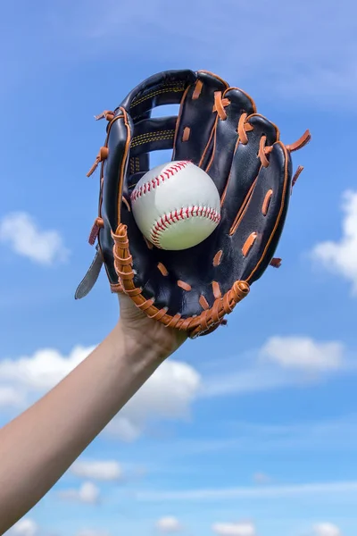 Arm holding baseball with glove  in blue sky — Stock Photo, Image