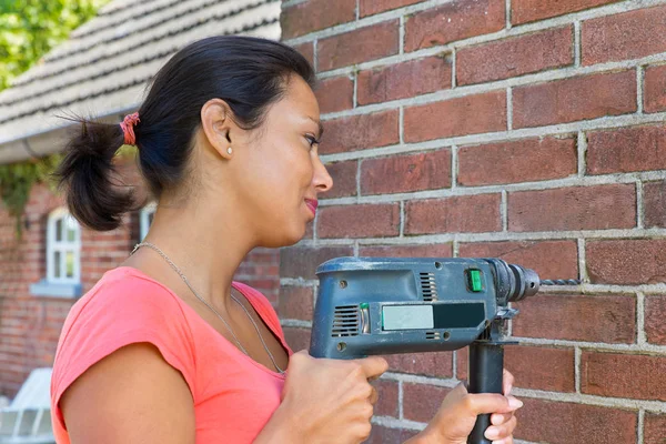 Vrouw met boren machine op bakstenen muur — Stockfoto