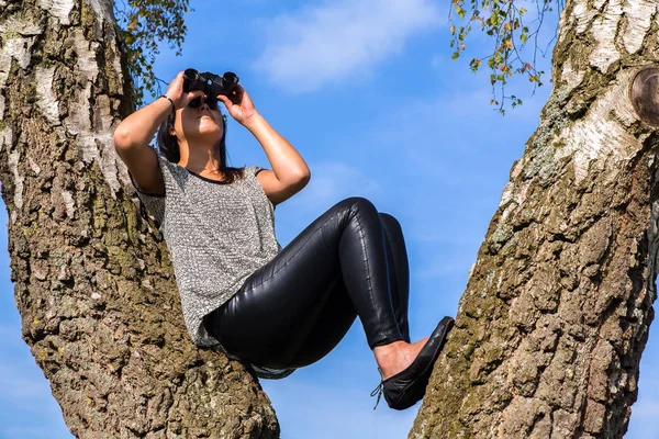 Mujer en árbol mirando a través de prismáticos — Foto de Stock
