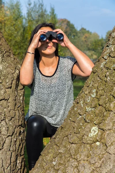 Frau blickt durch Fernglas in der Nähe von Baumstämmen — Stockfoto