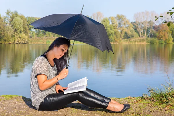 Vrouw met paraplu leesboek in de natuur — Stockfoto