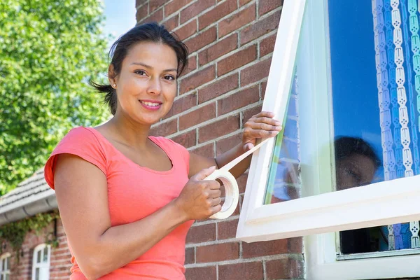 Женщина приклеивает клейкую ленту к стеклу окна — стоковое фото