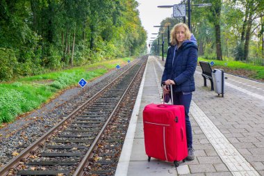 Bavullu Hollandalı kadın tren istasyonunda duruyor.