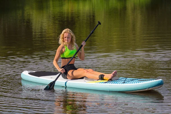 Сидяча молода жінка веслує зі СУП на воді — стокове фото
