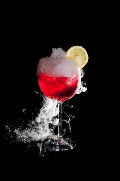 Una taza de cóctel rojo frío con humo de hielo seco y una rodaja de limón — Foto de Stock