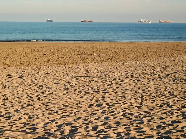 Gün batımında kumsalda deniz ve arka planda gemilerle