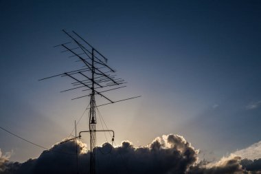 Mavi gökyüzündeki bulutların arasında bir antenin üzerinde güneş ışınları