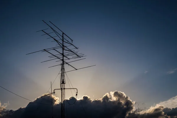 Mavi gökyüzündeki bulutların arasında bir antenin üzerinde güneş ışınları
