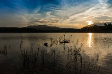 Güneş ışınları ve mavi bulutlu gökyüzü ile göle yansıyan unset manzara