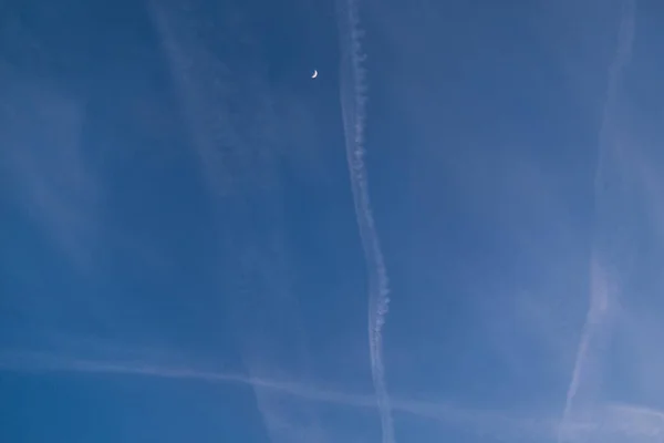 Crossing of airplane trails with crescent moon in blue sky