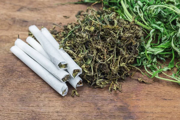 Marihuana sarma ve tütün beyaz kağıt üzerinde rulo hazır, ahşap kesme tahtası üzerinde.