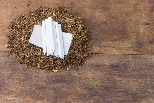 Siyah ahşap arka planda ve beyaz kağıtta sarmaya hazır tütün eklemleri. Üst görünüm.