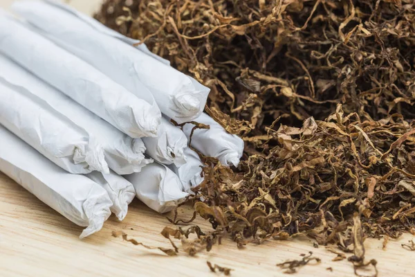 Ahşap arka planda ve beyaz kağıtta sarmaya hazır tütün eklemleri. Seçici Odaklanma.