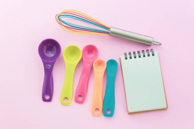 Bir çift tatlı pastel boyalı kaşık ve üst görüntüde pembe arka planda çırpma.