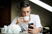 Mladý muž s mobilní pití kávy v kavárně
