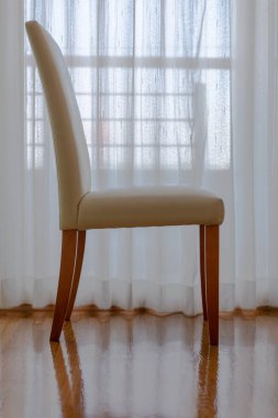 Beyaz odada tahta sandalyeler. Pencerenin yanındaki sandalyede ne var?