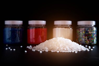 Siyah zemin üzerinde plastik şişelerde beyaz ve mavi plastik boncuklar, polimer boncuklar veya polimer reçine, polimer palet, petrokimya fabrikalarından alınmış ürünler..
