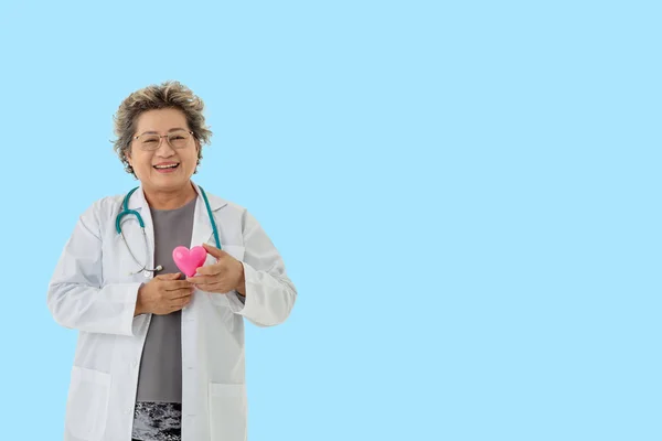 Senior woman doctor with stetoskop smile holding heart on blue — Stock fotografie