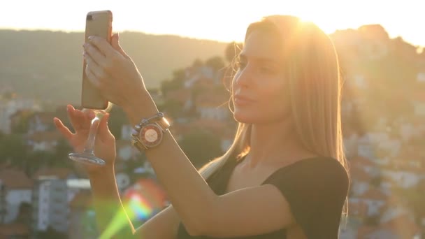 Pretty Blondynka Kobieta model z kieliszkiem do wina biorąc wideo ze smartfonem — Wideo stockowe