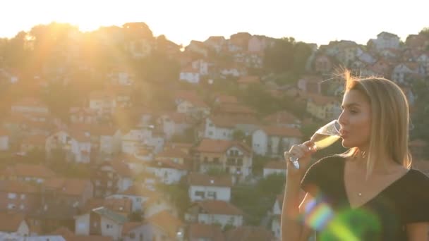 Vonzó női szőke modell ivóvíz pezsgő a tetőn, napfény háttérvilágítás — Stock videók