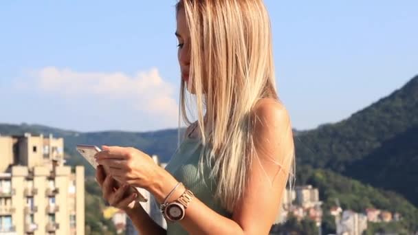 Giovane bella donna bionda utilizzando smartphone sul tetto il giorno soleggiato, primo piano — Video Stock