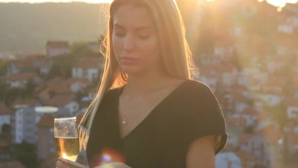 Jolie fille blonde modèle avec smartphone et champagne sous la lumière du soleil couchant — Video