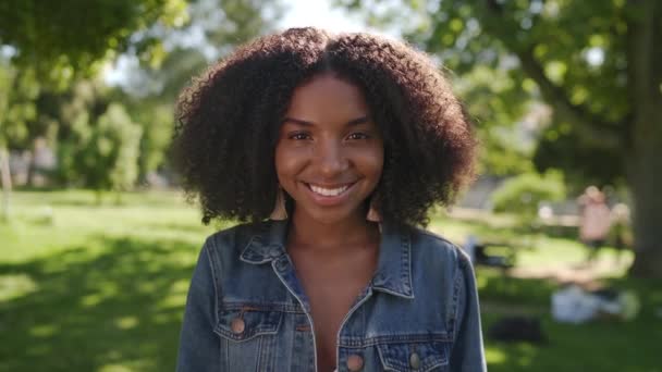 Egy fiatal afro-amerikai nő portréja áll a parkban, mosolyog és a kamerába néz. — Stock videók