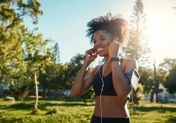 Wanita Afrika berkulit hitam muda yang bahagia menikmati mendengarkan musik menggunakan earphone sambil joging di bawah sinar matahari yang cerah di taman — Stok Foto