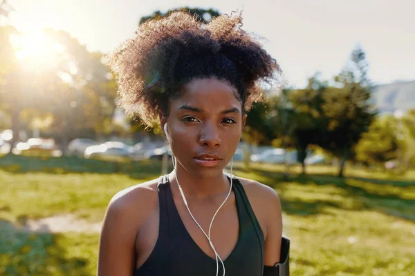 Retrato de una joven afroamericana deportiva con auriculares en los oídos escuchando música mirando a la cámara - decidida mujer negra fitness en el parque — Foto de Stock