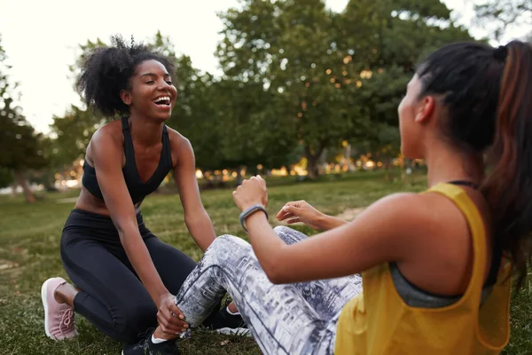 快乐而多样的年轻女性朋友们在公园的绿草上嬉笑，朋友们在户外锻炼时一起笑 — 图库照片