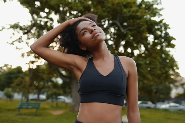 Retrato de uma jovem mulher negra em forma esticando o pescoço no parque antes de fazer exercício ao ar livre — Fotografia de Stock