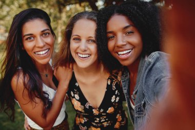 Bir grup mutlu, çok ırklı kız arkadaş güneşli bir günde parkta selfie çekiyorlar. - 