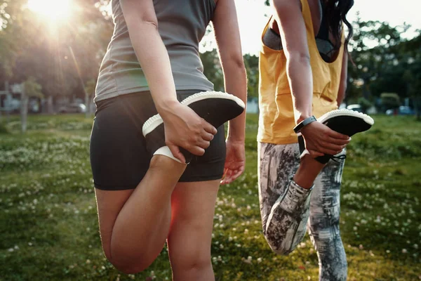 İki genç dişinin, koşmadan önce bacaklarını esneten iki spor kadının yakın çekimi. 
