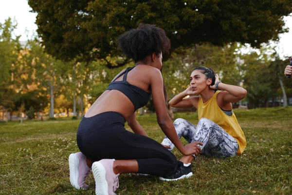 Ajuste mujer joven haciendo ejercicios crujientes con sus amigas durante el entrenamiento de atleta en el parque - mujer joven determinada y motivada haciendo ejercicio — Foto de Stock