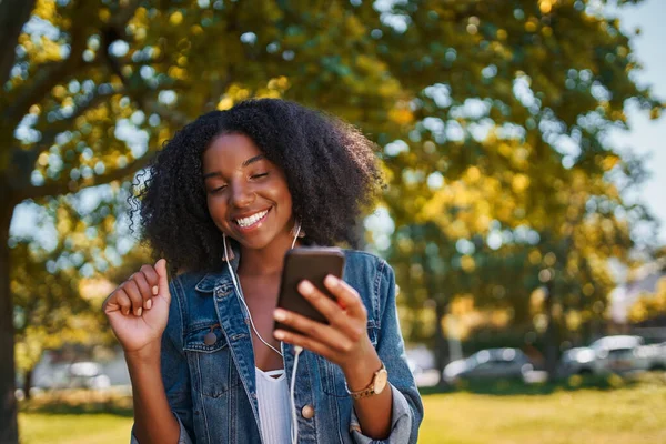 Afro-Amerikalı genç bir kadının portresi cep telefonuyla parkta müzik dinleyen, dans eden ve parkta eğlenen genç siyahi bir kadının kulaklıkla yaptığı müzik. — Stok fotoğraf