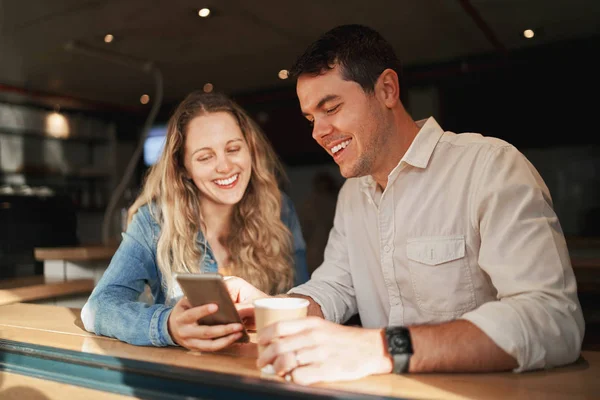 Adorável casal jovem sorridente na data apreciando navegar nos aplicativos móveis no balcão de café — Fotografia de Stock