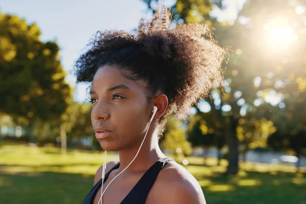 Primer plano de una joven afroamericana seria deportista parada en el parque escuchando música a través de auriculares - Mujer negra joven decidida — Foto de Stock