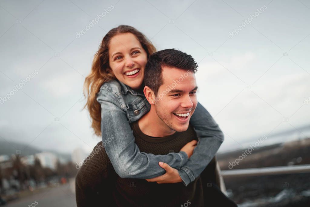 Smiling young man giving piggyback ride to his friend outdoors at the city street having fun together