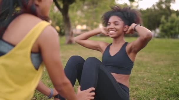 Junge Frau macht Sit-Ups mit Hilfe ihrer Freundin im Park - Freundinnen, die im Park Sport treiben und sich gegenseitig unterstützen — Stockvideo