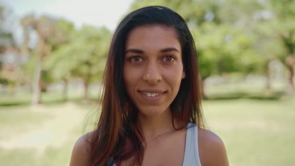 Portraitaufnahme einer gut aussehenden Mischlingsrasse brünette junge Frau, die vor der Kamera steht und in sie hineinlächelt - glückliches Mädchen an einem Sommertag — Stockvideo
