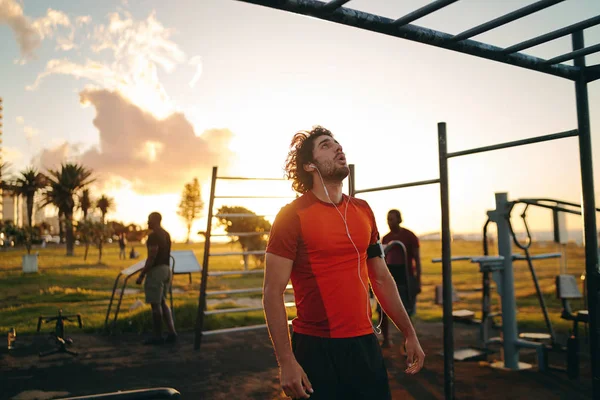 Joven deportivo con auriculares en los oídos mirando a los bares de monos para hacer ejercicio en el parque del gimnasio - Hombre motivándose a hacer ejercicios —  Fotos de Stock