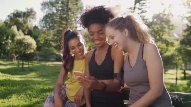 Çeşitli sportif genç bayan arkadaşlar sabah parkta bir bankta oturup cep telefonuna bakıyorlar. Cep telefonuyla konuşan bir grup bayan arkadaş.