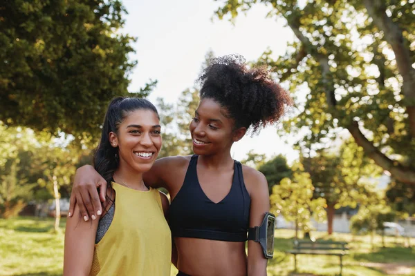 Leende unga kvinnor i sportkläder stående arm i arm tillsammans i parken - leende multietniska fitness vänner i parken — Stockfoto